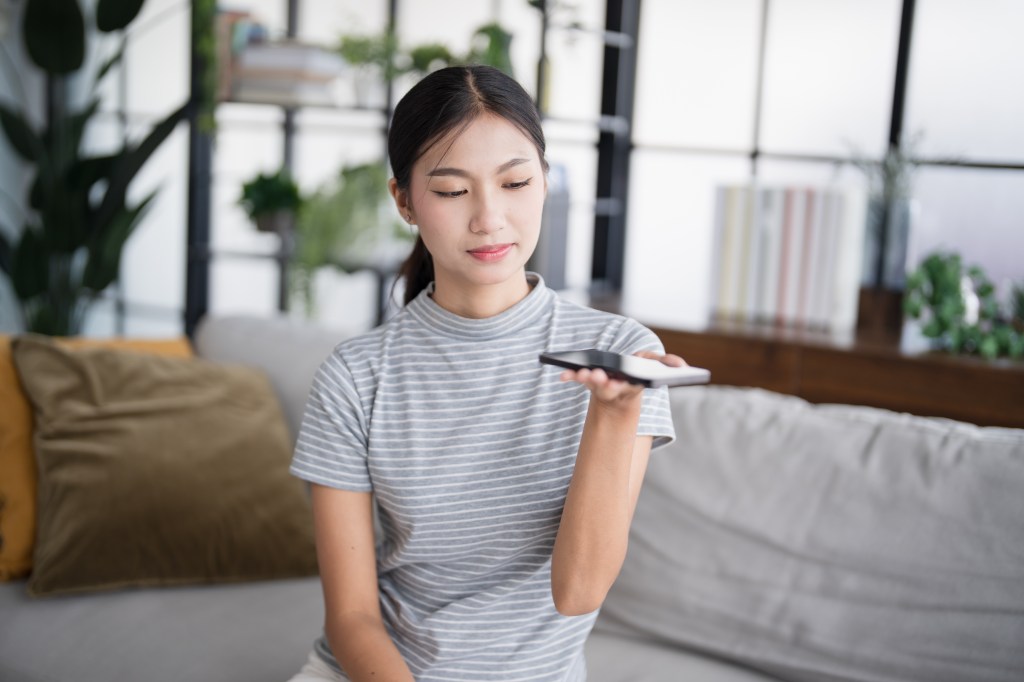 Asian woman at home engaging with voice assistant on her smartphone