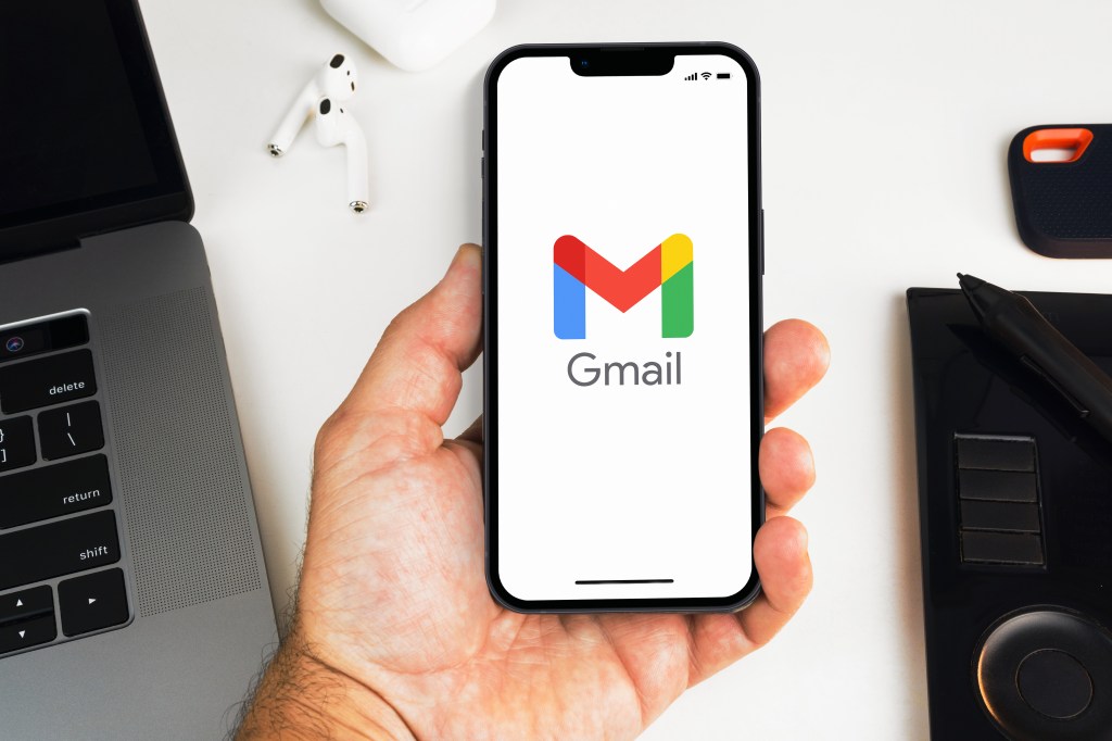 Male hand holding a smartphone displaying the Google Gmail app interface in an office environment