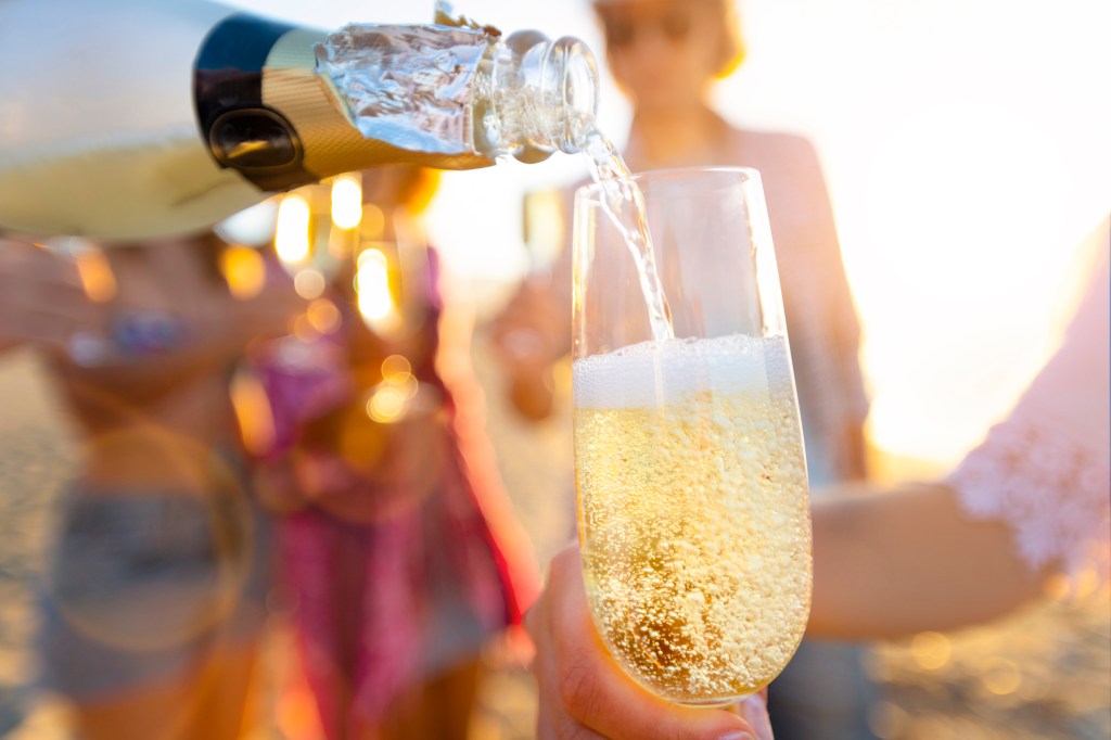 Pouring a glass of champagne with people sharing in the background. The holiday is on the beach in the sunset. close up